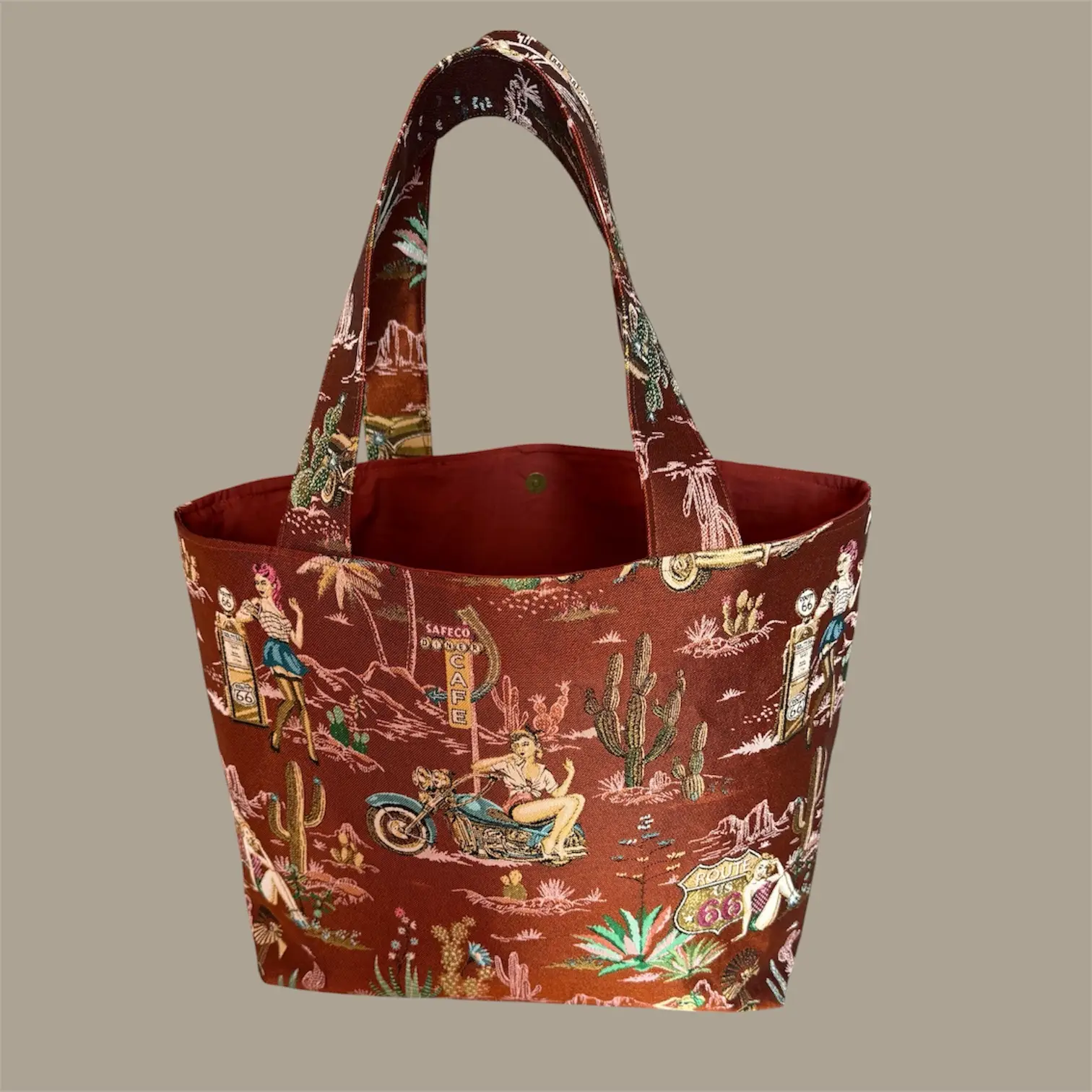 Red-brown tote bag with a retro desert scene print, showing cacti, riders, and Route 66 signage.